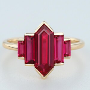 May include: A gold ring featuring a cluster of vibrant red gemstones. The central, elongated gemstone is flanked by four smaller, rectangular stones, all set in a geometric design. The ring's band is a simple, polished gold.