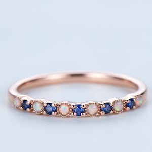 May include: Rose gold ring with alternating opal and sapphire gemstones. The ring features a delicate band and a row of small, round gemstones in a repeating pattern of light pink and deep blue.