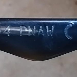 May include: Close-up of a dark blue eyeglass arm. The text "W2954 PNAW CE" is etched in white on the arm. The arm has a curved, triangular shape.