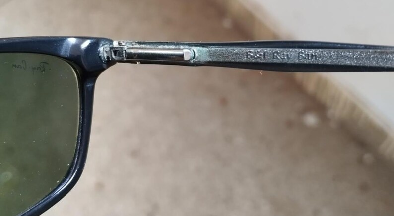 May include: Close-up of a pair of sunglasses with a dark blue frame and green lenses. The arm of the glasses has the text "B&L Ray 601" printed on it. The Ray-Ban logo is visible on the lens.