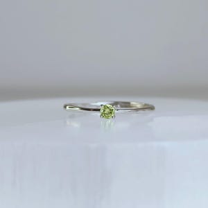 May include: A delicate silver ring featuring a small, square-cut, light green gemstone. The ring has a thin band and a simple, elegant design. The gemstone is the focal point, set in a minimalist style, perfect for everyday wear.