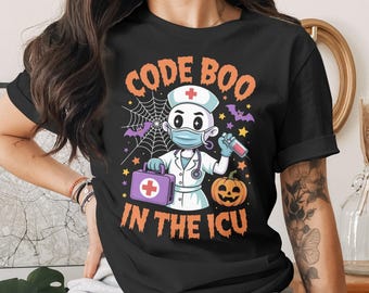 Pode incluir: Camiseta preta com um gráfico temático de Halloween. O design apresenta uma enfermeira de desenho animado com máscara, segurando uma seringa e uma bolsa médica, com o texto "CODE BOO IN THE ICU". Uma abóbora, morcegos e teias de aranha completam o design.