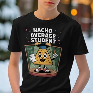 Peut inclure: T-shirt noir avec l'inscription "NACHO AVERAGE STUDENT" et un personnage de chips nacho de dessin animé portant une toque de diplômé. Le nacho tient un crayon et un bloc-notes devant un tableau noir. Le motif comprend des confettis colorés.