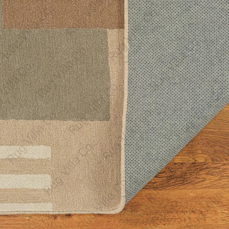 K&ouml;nnte beinhalten: Ein rechteckiger Teppich mit einem geometrischen Muster in Braun-, Beige- und Gr&uuml;nt&ouml;nen. Die Unterseite des Teppichs ist hellgrau mit einer gepunkteten Textur. Der Teppich ist teilweise aufgerollt und gibt den Blick auf den Holzboden frei.