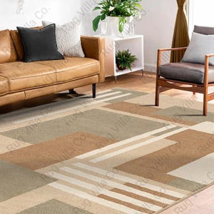 K&ouml;nnte beinhalten: Geometrisch gemusterter Teppich in Beige-, Braun- und Gr&uuml;nt&ouml;nen. Der Teppich hat ein modernes Design mit rechteckigen und linearen Formen. Der Teppich befindet sich in einem Wohnzimmer mit einem Ledersofa und einem Holzstuhl.