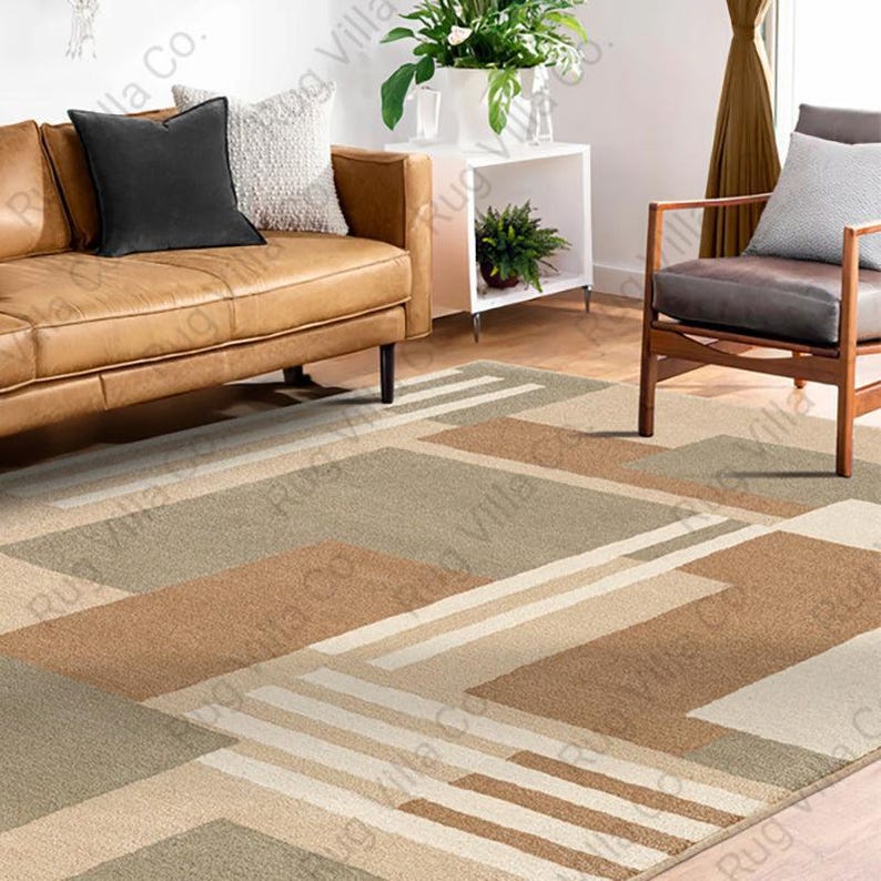 K&ouml;nnte beinhalten: Geometrisch gemusterter Teppich in Beige-, Braun- und Gr&uuml;nt&ouml;nen. Der Teppich hat ein modernes Design mit rechteckigen und linearen Formen. Der Teppich befindet sich in einem Wohnzimmer mit einem Ledersofa und einem Holzstuhl.