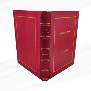 Może przedstawiać: Twarda oprawa książki zatytułowana "The Red Book" autorstwa C.G. Junga. Książka ma żywą czerwoną okładkę ze złotymi literami i detalami. Grzbiet jest r&oacute;wnież czerwony ze złotymi akcentami. Książka jest otwarta.