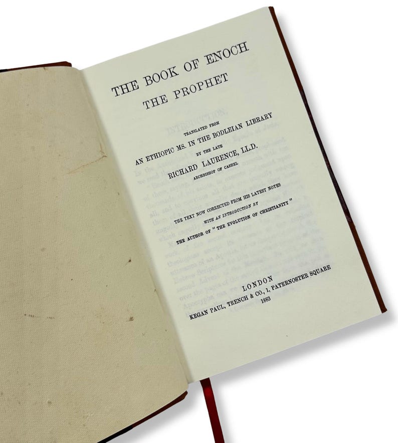 May include: An open book titled "THE BOOK OF ENOCH THE PROPHET" with text in black font. The book's pages are off-white, and the cover is a dark reddish-brown. A red ribbon bookmark is visible. The text includes the translator's name and the publisher's location.