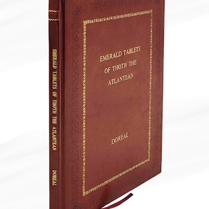 Puede incluir: Un libro de tapa dura burdeos titulado "Emerald Tablets of Thoth the Atlantean" de DOREAL. El libro tiene letras doradas y bordes decorativos. Se ve una cinta de marcador burdeos.