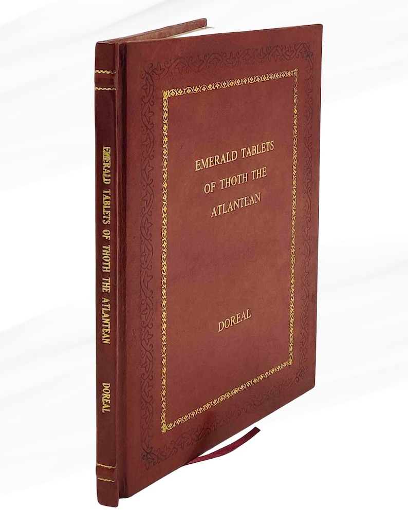 Puede incluir: Un libro de tapa dura burdeos titulado "Emerald Tablets of Thoth the Atlantean" de DOREAL. El libro tiene letras doradas y bordes decorativos. Se ve una cinta de marcador burdeos.