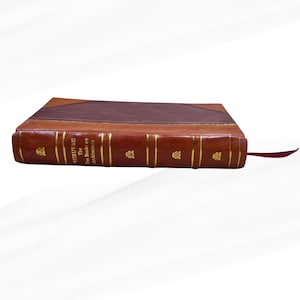 May include: A leather-bound book with gold lettering and a maroon bookmark. The book's cover is a rich brown, with a darker brown section at the top. The spine features the title "VITRUVIUS: The Ten Books on Architecture."