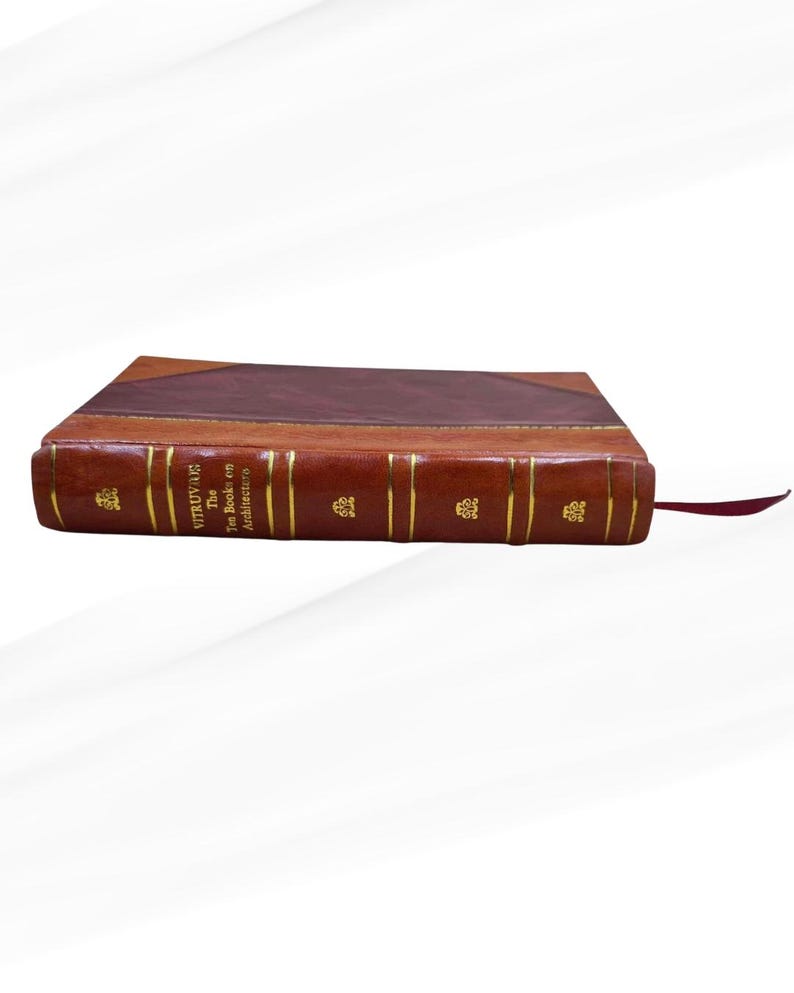 May include: A leather-bound book with gold lettering and a maroon bookmark. The book's cover is a rich brown, with a darker brown section at the top. The spine features the title "VITRUVIUS: The Ten Books on Architecture."