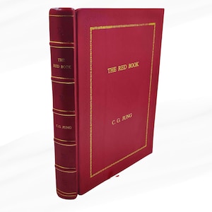 Może przedstawiać: Czerwona książka zatytułowana "THE RED BOOK" autorstwa C.G. Junga. Książka ma złote obramowanie i złote litery. Grzbiet jest r&oacute;wnież czerwony ze złotymi literami i detalami. Książka stoi pionowo.