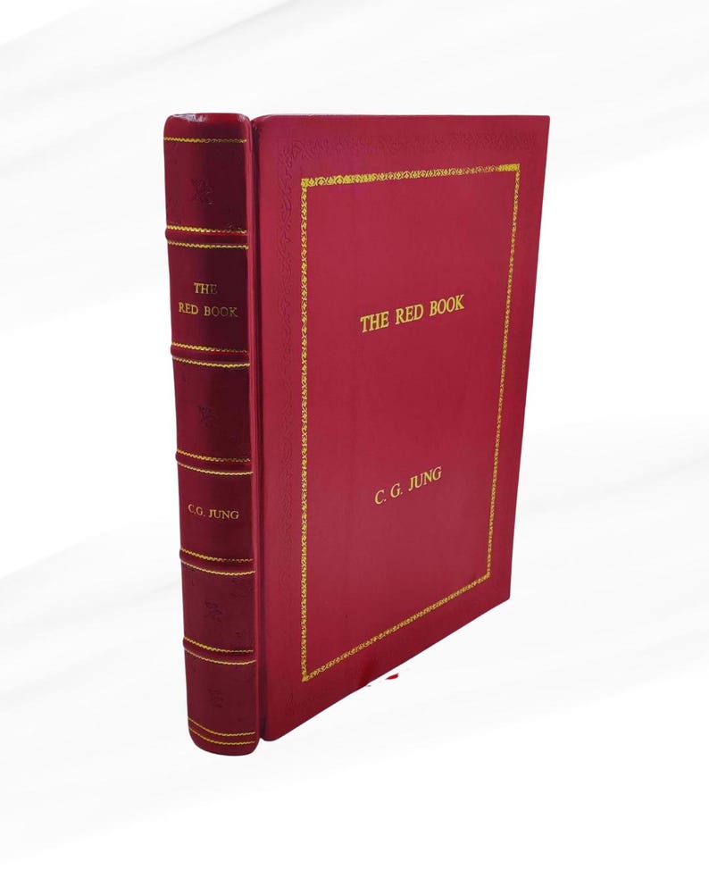 Może przedstawiać: Czerwona książka zatytułowana "THE RED BOOK" autorstwa C.G. Junga. Książka ma złote obramowanie i złote litery. Grzbiet jest r&oacute;wnież czerwony ze złotymi literami i detalami. Książka stoi pionowo.