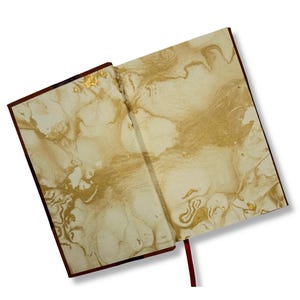 May include: Open journal with a cream-colored marbled design and gold accents. The journal has a dark brown cover and a red ribbon bookmark. The pages are open, displaying the intricate pattern.