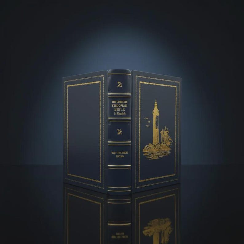 K&ouml;nnte beinhalten: Ein marineblaues Buch mit goldenen Akzenten, betitelt "The Complete Ethiopian Bible in English". Das Cover zeigt eine goldene Illustration eines Leuchtturms und eines Schiffes. Das Buch ist ge&ouml;ffnet und zeigt den Buchr&uuml;cken und die Innenseite des Covers.