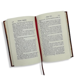 May include: An open book with a red ribbon bookmark. The pages display printed text, with the title "Marcus Aurelius" on the left and "Book VII" on the right. The book has a dark brown cover.