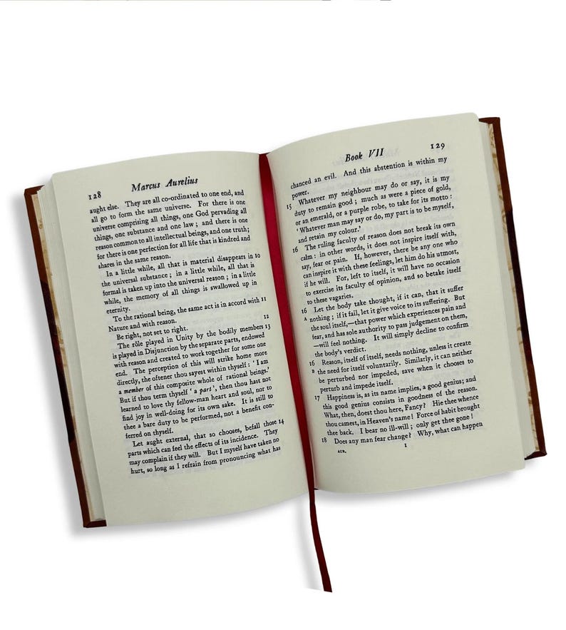May include: An open book with a red ribbon bookmark. The pages display printed text, with the title "Marcus Aurelius" on the left and "Book VII" on the right. The book has a dark brown cover.