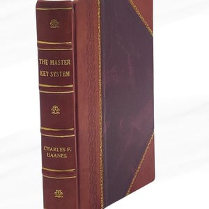 Op de afbeelding: Een hardcover boek getiteld "THE MASTER KEY SYSTEM" van Charles F. Haanel. Het boek heeft een bordeauxrode leren kaft met gouden accenten en reliëf bloemmotieven. De rug is een donkerdere tint bordeaux.
