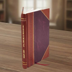 Puede incluir: Un libro de tapa dura titulado "THE DEVOTION TO THE HOLY FACE" de Abbe Janvier. El libro tiene una cubierta burdeos con un panel morado oscuro y detalles dorados. Se ve una cinta roja como marcapáginas.