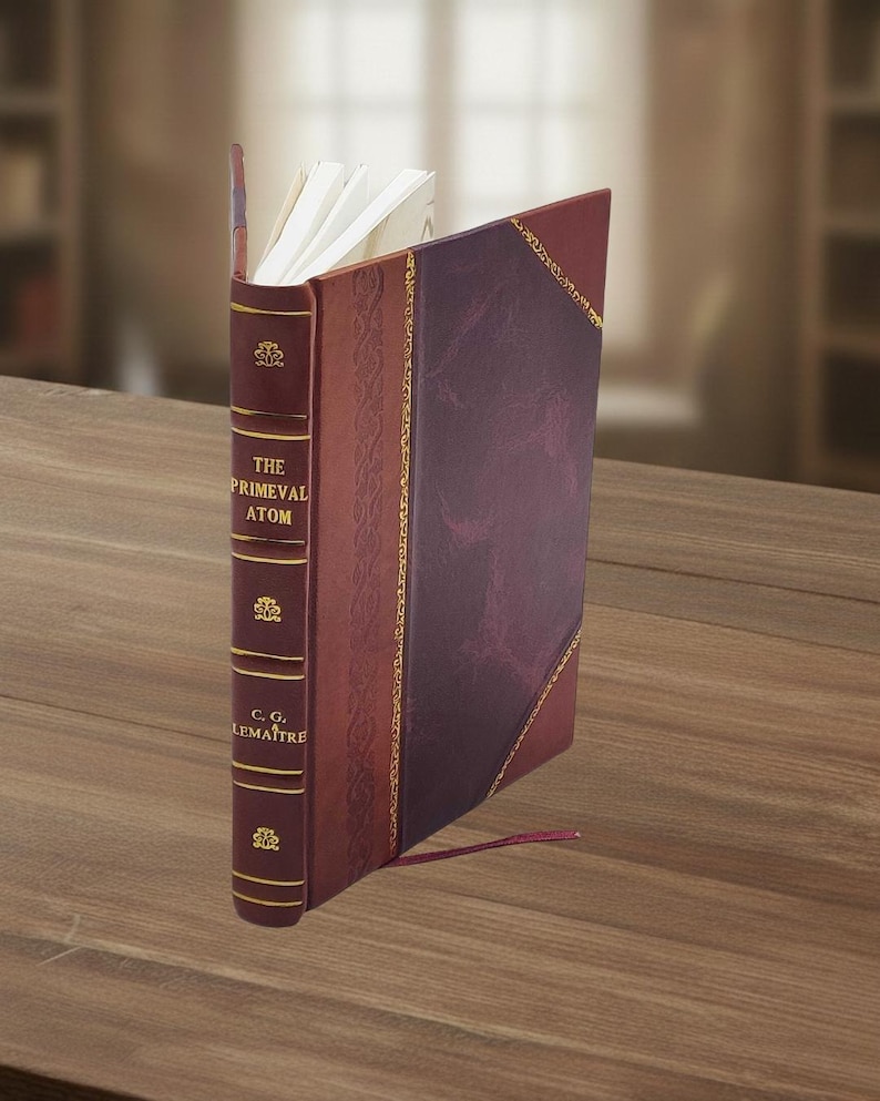 May include: A hardcover book titled "The Primeval Atom" by C.G. Lema&icirc;tre. The book has a burgundy leather cover with gold accents and a decorative spine. The pages are white, and a red ribbon bookmark is visible.