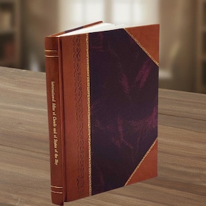 Puede incluir: Un libro de tapa dura con una cubierta de cuero marrón y un panel central burdeos. La columna vertebral presenta el texto "International Atlas of Clouds and of States of the Sky". Una cinta roja como marcapáginas sobresale del libro.