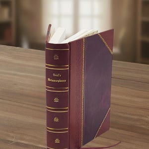 Op de afbeelding: Een hardcover boek getiteld Ovid's Metamorphoses met een diepbordeauxrode rug voorzien van gouden horizontale lijnen en kleine gouden bloememblemen. De kaft is donkerpaars met een gouden decoratieve rand en een dun bordeauxrood leeslint.