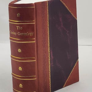 May include: A hardback book titled "The Cooley Genealogy." The book has a dark red leather cover with gold accents and decorative patterns. The spine features the title in gold lettering and decorative floral emblems.
