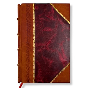 May include: A leather-bound journal with a rich, textured appearance. The cover features a deep burgundy diamond-shaped panel framed by gold accents, set against a warm brown background. A decorative gold border and a red ribbon bookmark add to the classic design.