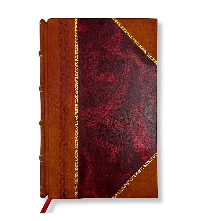 May include: A leather-bound journal with a rich, textured appearance. The cover features a deep burgundy diamond-shaped panel framed by gold accents, set against a warm brown background. A decorative gold border and a red ribbon bookmark add to the classic design.
