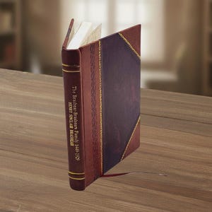 May include: A hardcover book with a burgundy leather spine and cover, featuring gold accents and the title "The Brashear-Brashears Family 1449-1929." The book is open, revealing white pages, and rests on a wooden surface.