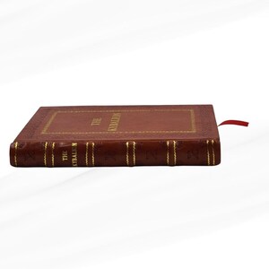 Pode incluir: Um livro de capa dura intitulado "The Kybalion" com capa de couro marrom e letras douradas. O livro tem uma borda decorativa e uma fita vermelha como marcador. A lombada tamb&eacute;m apresenta letras douradas.