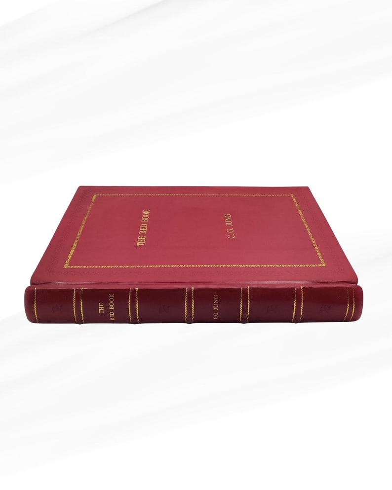 Może przedstawiać: Twarda książka w kolorze czerwonym zatytułowana "THE RED BOOK" autorstwa C.G. Junga. Książka ma złote litery i złotą obw&oacute;dkę. Grzbiet r&oacute;wnież ma złote litery. Książka jest wyświetlana na białym tle.