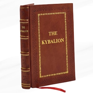 Op de afbeelding: Een hardcover boek getiteld "THE KYBALION" met een bruine leren kaft en gouden letters. De kaft heeft een gouden decoratieve rand. Een rood lint-bladwijzer steekt uit de rug van het boek.