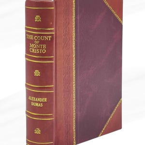 May include: A burgundy leather-bound book titled "The Count of Monte Cristo" by Alexander Dumas. The cover and spine feature gold detailing. A red ribbon bookmark is visible. The book is a classic.