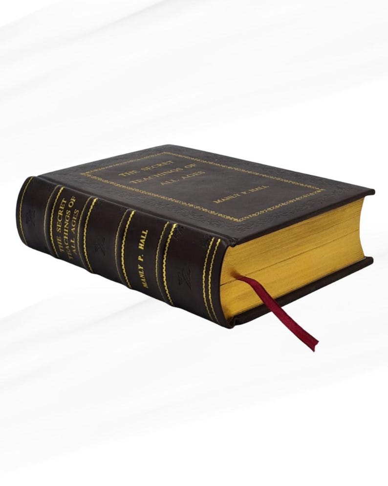 May include: A hardcover book titled "The Secret Teachings of All Ages" by Manly P. Hall. The book has a dark brown cover with gold lettering and gold-gilded pages. A red ribbon bookmark is inserted.