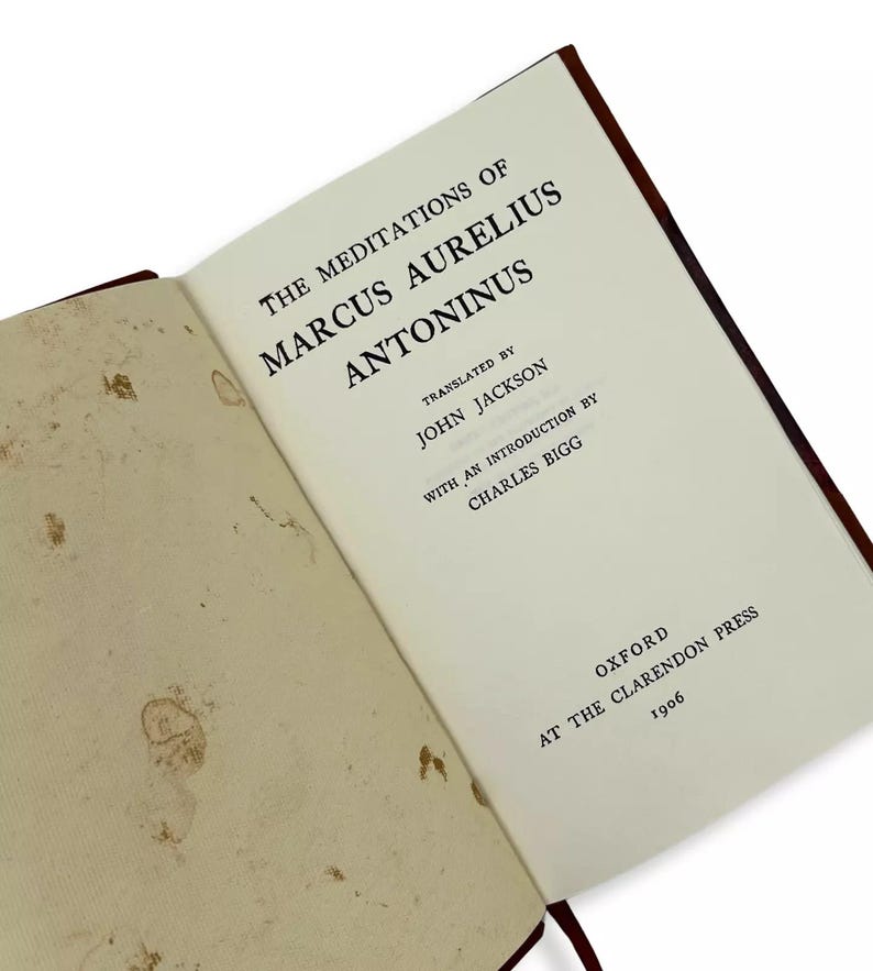 May include: An open book titled "The Meditations of Marcus Aurelius Antoninus" with text in black font. The book is translated by John Jackson and published by Oxford at the Clarendon Press in 1906. The pages are off-white with brown spots.