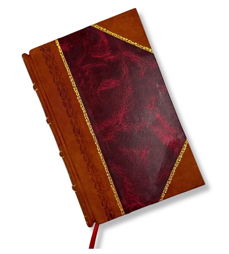 May include: A leather-bound journal with a burgundy cover and gold trim. The journal has a decorative border on the spine and a red ribbon bookmark. The cover is a rich brown color.