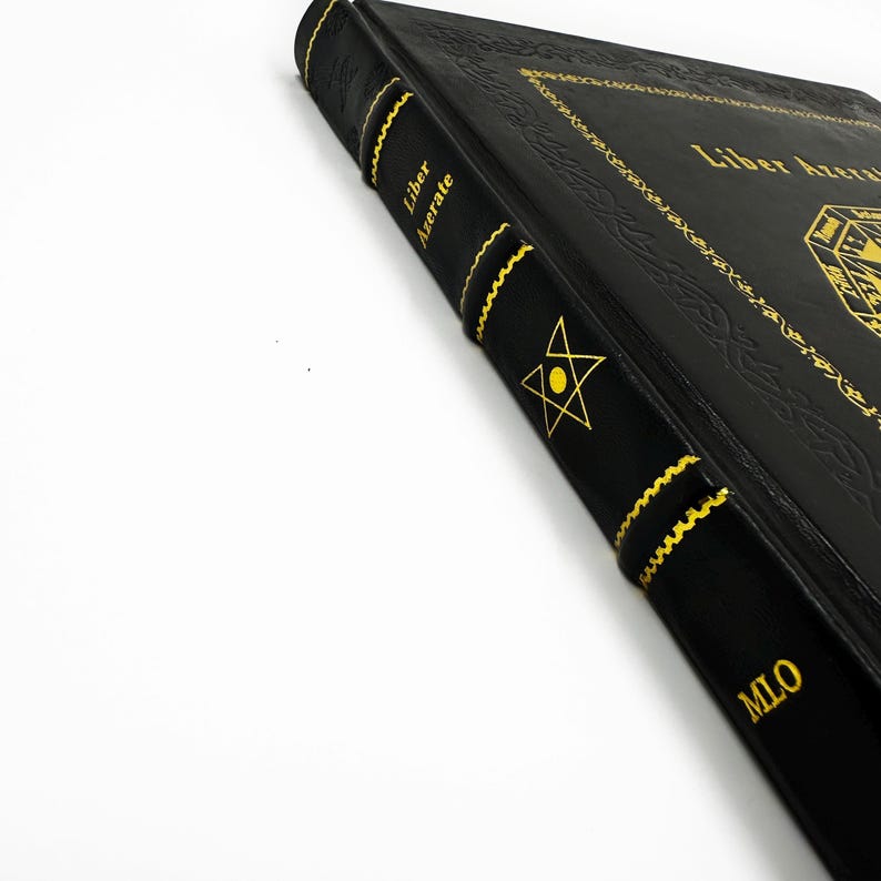 May include: Black book with gold lettering and accents. The spine features the text "Liber Azerate" and a star symbol. The cover has ornate gold designs and the title "Liber Azerate". The book's edges are also accented with gold.