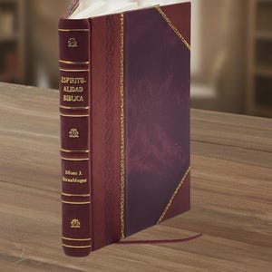 May include: A burgundy leather-bound book with gold detailing. The spine displays the title "ESPIRITUALIDAD BIBLICA" and the author's name, Mons J. Straubinger. The book is resting on a wooden table.