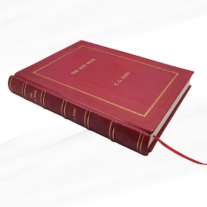 Może przedstawiać: Czerwona książka w twardej oprawie zatytułowana "THE RED BOOK" autorstwa C.G. Junga. Książka ma złote litery i złotą obw&oacute;dkę. Czerwona wstążka służy jako zakładka.