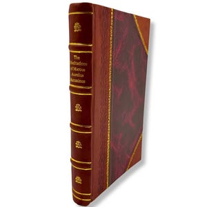 May include: A hardcover book titled "The Meditations of Marcus Aurelius Antoninus." The book has a burgundy leather cover with gold accents and a decorative spine. The edges of the pages are also gold.