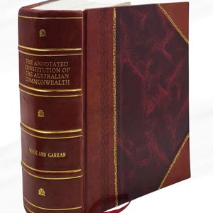 Könnte beinhalten: Ein gebundenes Buch mit dem Titel "THE ANNOTATED CONSTITUTION OF THE AUSTRALIAN COMMONWEALTH" von Quick und Garran. Der Einband ist aus burgunderfarbenem Leder mit goldenen Verzierungen. Ein rotes Leseband ist sichtbar.