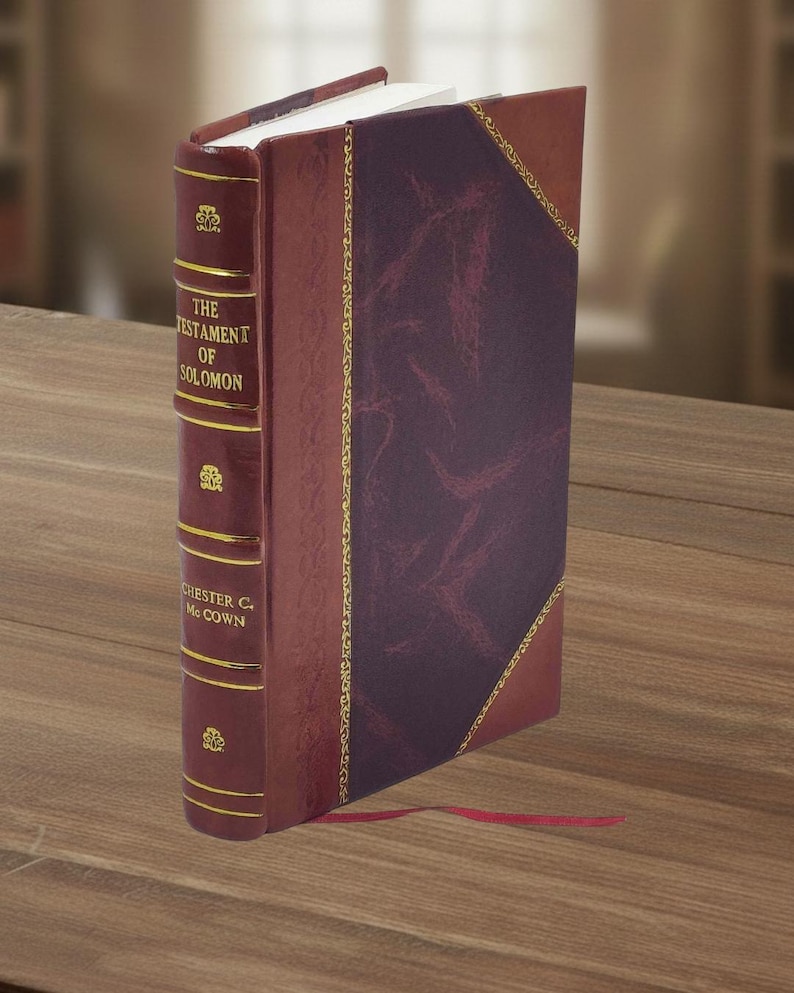 May include: A hardcover book titled "The Testament of Solomon" with a burgundy leather cover and gold lettering. The spine features decorative gold accents and the author's name. A red ribbon bookmark extends from the pages.