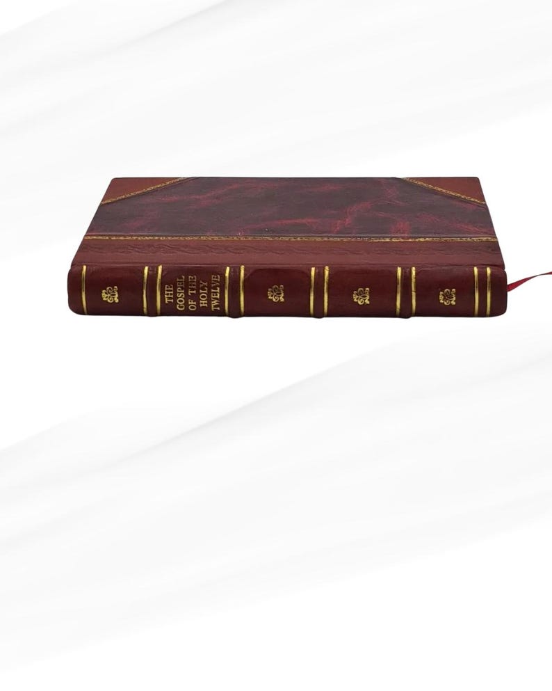 May include: A burgundy leather-bound book with gold detailing. The spine displays the title "THE GOSPEL OF THE HOLY TWELVE" in gold. A red ribbon bookmark is inserted. The book has a classic, elegant design.