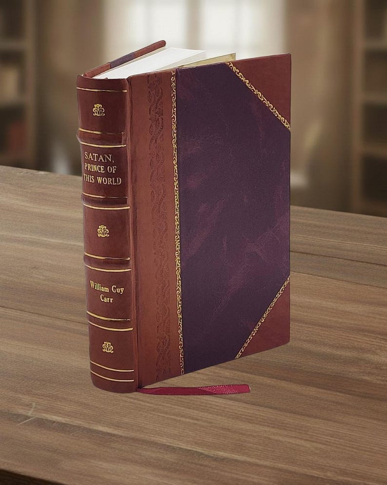 May include: A hardcover book titled "SATAN, PRINCE OF THIS WORLD" by William Guy Carr. The book has a burgundy leather cover with gold accents and a purple panel. A red ribbon bookmark is visible.