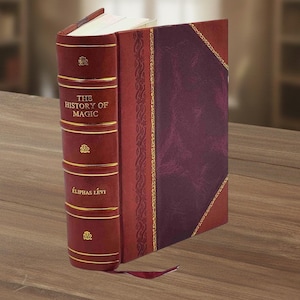 Puede incluir: Un libro encuadernado en cuero burdeos titulado "THE HISTORY OF MAGIC" de &Eacute;LIPHAS L&Eacute;VI. El libro presenta detalles dorados y un lomo decorativo. Est&aacute; sobre una superficie de madera.