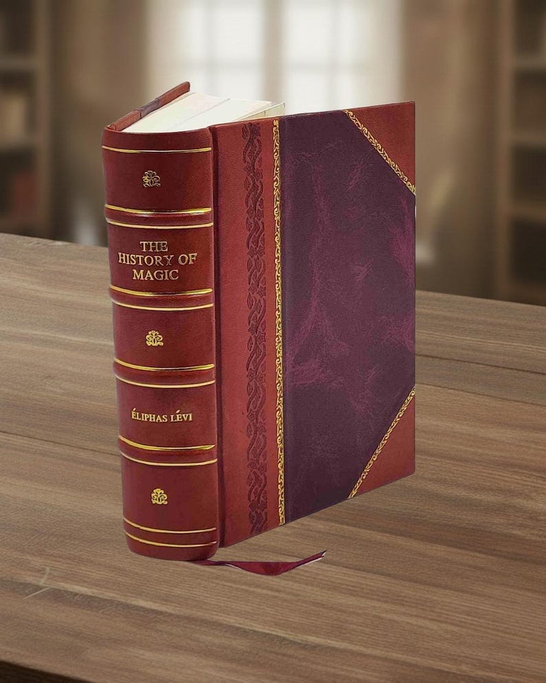 Puede incluir: Un libro encuadernado en cuero burdeos titulado "THE HISTORY OF MAGIC" de &Eacute;LIPHAS L&Eacute;VI. El libro presenta detalles dorados y un lomo decorativo. Est&aacute; sobre una superficie de madera.
