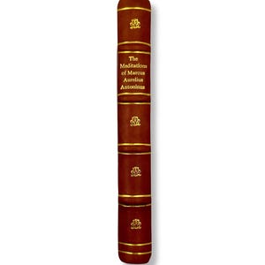 May include: A hardcover book with a dark brown leather cover. The spine features gold lettering that reads "The Meditations of Marcus Aurelius Antoninus." Gold bands and decorative emblems adorn the spine.