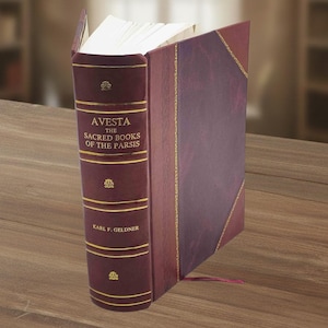 Pode incluir: Um livro de capa dura marrom-avermelhado intitulado "AVESTA The Sacred Books of the Parsis" com letras e detalhes dourados. O livro está aberto, revelando páginas brancas, e tem uma fita de marcador marrom-avermelhada. O livro está em uma superfície de madeira.